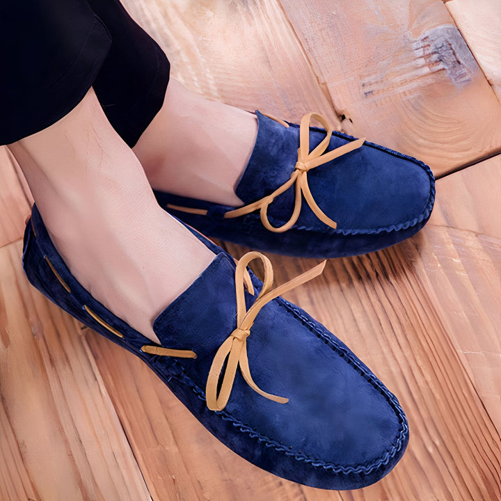 Mocassins pour hommes en daim bleu marine avec lacets décoratifs beiges, posés sur un parquet en bois clair. Chaussures décontractées, confort et élégance., 45287109853365,45287110082741,45287110115509,45287110148277,45287110181045,45287110213813,45287110246581