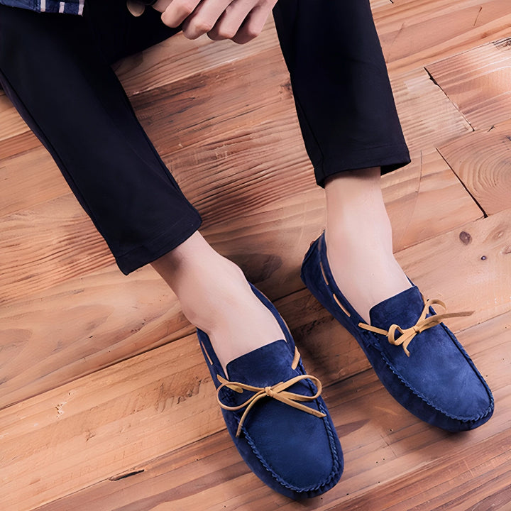 Gros plan de mocassins bleus en daim avec des lacets en cuir beige, portés par une personne assise sur un plancher en bois. Style décontracté et élégant, parfait pour un look tendance., 45287109853365,45287110082741,45287110115509,45287110148277,45287110181045,45287110213813,45287110246581