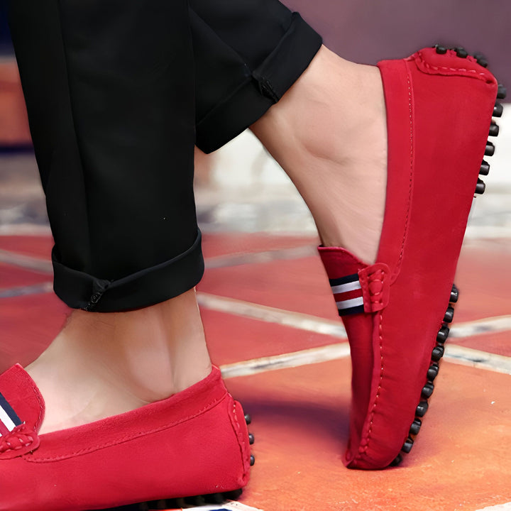 Gros plan sur des mocassins rouges en daim portés avec un pantalon noir. Détails incluent des rayures décoratives et une semelle à picots. Chaussures de style décontracté pour homme., 45287104381109,45287104413877,45287104446645,45287104479413,45287104512181,45287104544949,45287104577717,45287104610485,45287104643253,45287104676021,45287104708789,45287104741557