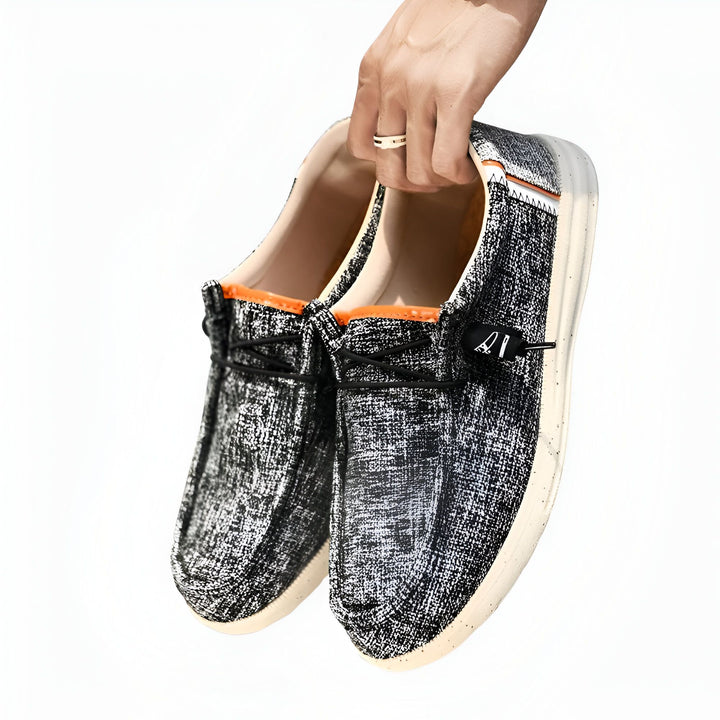 Une main tenant une paire de chaussures décontractées en toile grise et blanche, avec des lacets noirs et une doublure intérieure orange. Les chaussures ont des semelles blanches et un design sans talon., 45286690422965,45286690455733,45286690488501,45286690521269,45286690554037,45286690586805,45286690619573,45286690652341,45286690685109,45286690717877,45286690750645,45286690783413,45286690816181,45286690848949,45286690881717,45286690914485,45286690947253,45286690980021,45286691012789,45286691045557,45