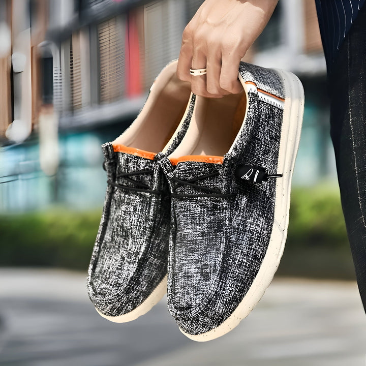 Un homme tient une paire de chaussures décontractées à enfiler, en tissu texturé noir et blanc, avec une doublure orange. Elles ont des lacets élastiques noirs et une semelle blanche. Idéal pour un style relax et moderne., 45286690422965,45286690455733,45286690488501,45286690521269,45286690554037,45286690586805,45286690619573,45286690652341,45286690685109,45286690717877,45286690750645,45286690783413,45286690816181,45286690848949,45286690881717,45286690914485,45286690947253,45286690980021,45286691012