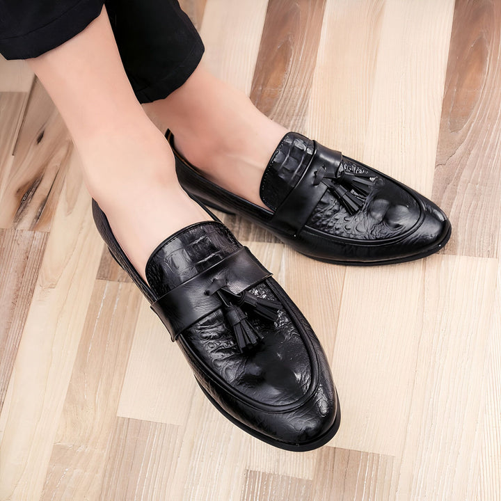 Homme portant des mocassins en cuir noir à glands, avec un motif texturé effet croco. Chaussures élégantes et raffinées sur un parquet en bois clair., 45286935756981,45286935789749,45286935822517,45286935855285,45286935888053,45286935920821,45286935953589,45286935986357,45286936019125,45286936051893,45286936084661,45286936117429,45286936150197,45286936182965,45286936215733,45286936248501,45286936281269,45286936314037,45286936346805,45286936379573