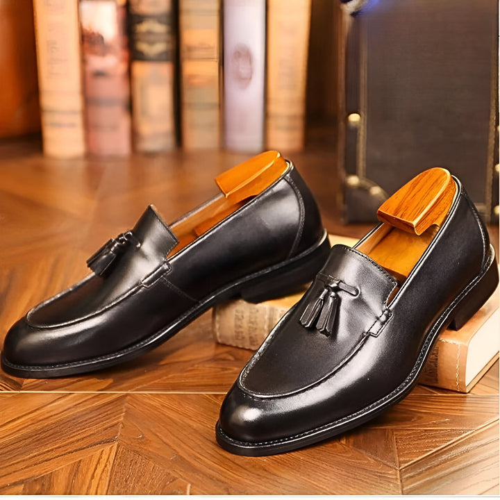 Image de deux mocassins noirs élégants avec des glands, reposant sur des livres. Ils sont accompagnés d'embauchoirs en bois. L'arrière-plan est flou avec d'autres livres et un coffre vintage. Idéal pour un look sophistiqué et raffiné., 45286723518645,45286723551413,45286723584181,45286723616949,45286723649717,45286723682485,45286723715253,45286723748021,45286723780789,45286723813557,45286723846325,45286723879093,45286723911861,45286723944629