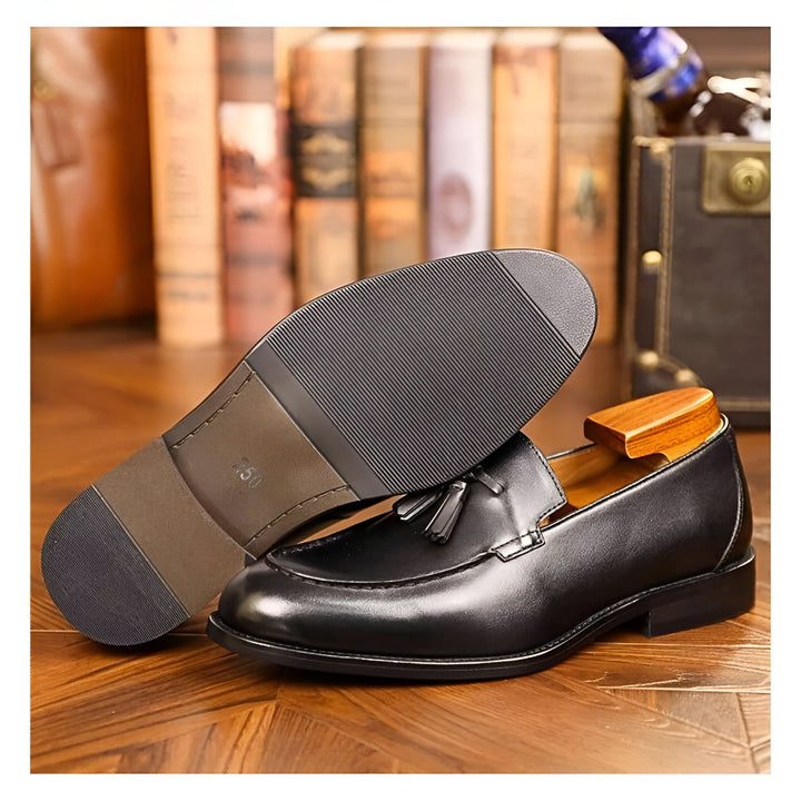 Chaussures pour hommes en cuir noir, modèle mocassins à glands. Semelle en cuir visible à côté. Fond avec des livres et valise vintage. Élégance masculine, style classique et intemporel. Accessoires de mode, chaussures de qualité., 45286723518645,45286723551413,45286723584181,45286723616949,45286723649717,45286723682485,45286723715253,45286723748021,45286723780789,45286723813557,45286723846325,45286723879093,45286723911861,45286723944629