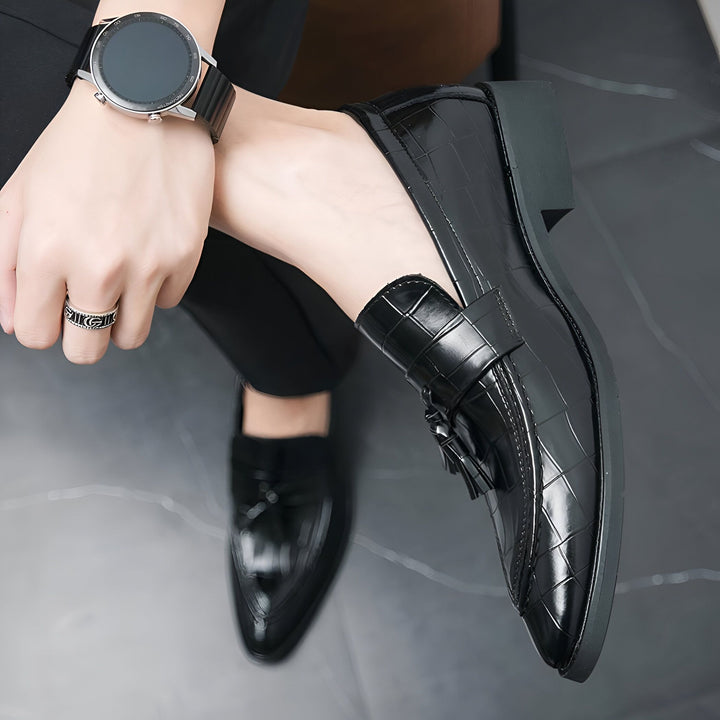Gros plan sur une personne portant des mocassins en cuir noir texturé, une montre connectée à bracelet en cuir noir et une bague en argent. Le style est élégant et soigné., 45287072923829,45287072956597,45287072989365,45287073022133,45287073054901,45287073087669,45287073120437,45287073153205,45287073185973