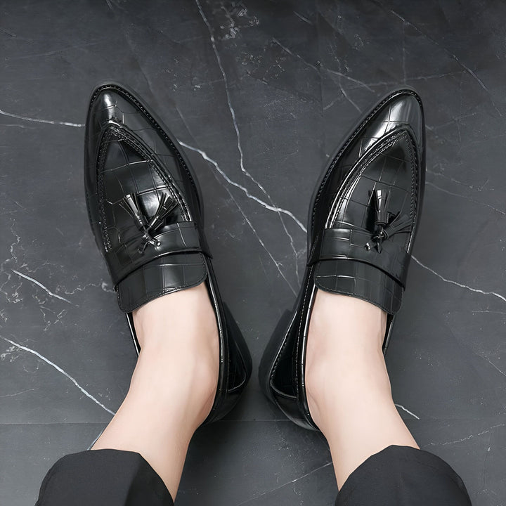 Vue de dessus de mocassins noirs en cuir verni avec des glands décoratifs, portés par une personne. Les chaussures ont un motif texturé crocodile et reposent sur un sol en marbre noir., 45287072923829,45287072956597,45287072989365,45287073022133,45287073054901,45287073087669,45287073120437,45287073153205,45287073185973