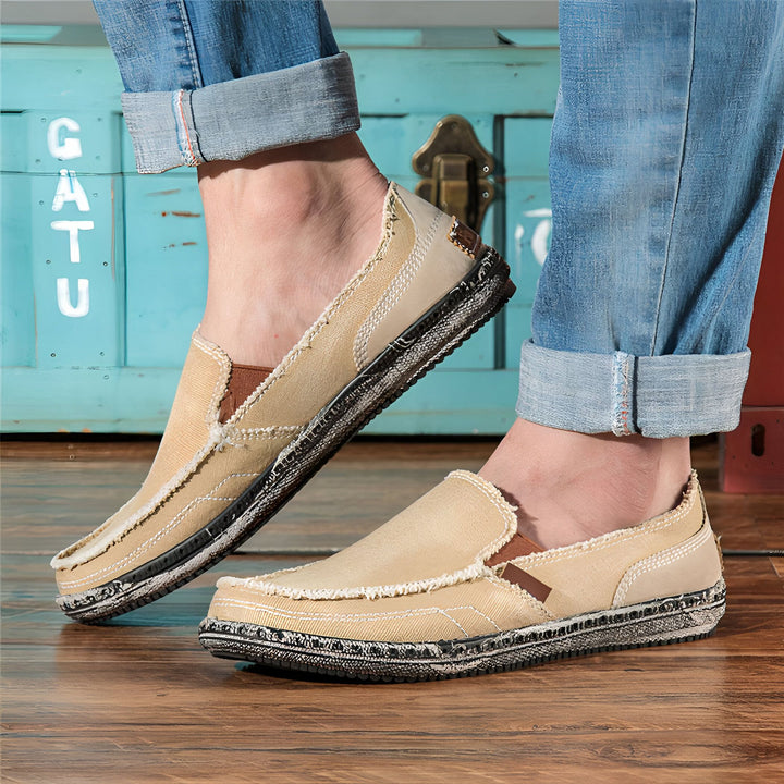 Homme portant des mocassins en toile beiges avec des jeans retroussés, devant une malle bleue. Chaussures décontractées pour hommes. Mode masculine., 45286737084597,45286737117365,45286737150133,45286737182901,45286737215669,45286737248437,45286737281205,45286737313973,45286737346741,45286737379509,45286737412277,45286737445045,45286737477813,45286737510581,45286737543349,45286737576117,45286737608885,45286737641653,45286737674421,45286737707189,45286737739957,45286737772725,45286737805493,452867378382