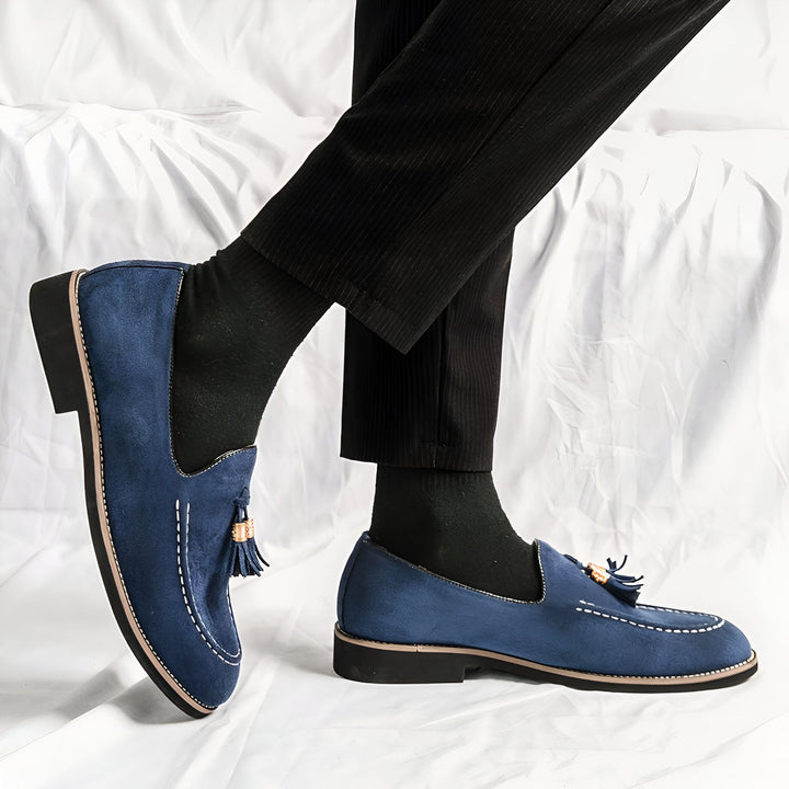 Gros plan sur des chaussures de ville bleues en daim avec glands dorés, portées avec un pantalon noir sur un fond blanc texturé. Chaussures élégantes pour hommes., 45287109394613,45287109427381,45287109460149,45287109492917,45287109525685,45287109558453,45287109591221,45287109623989,45287109656757,45287109689525
