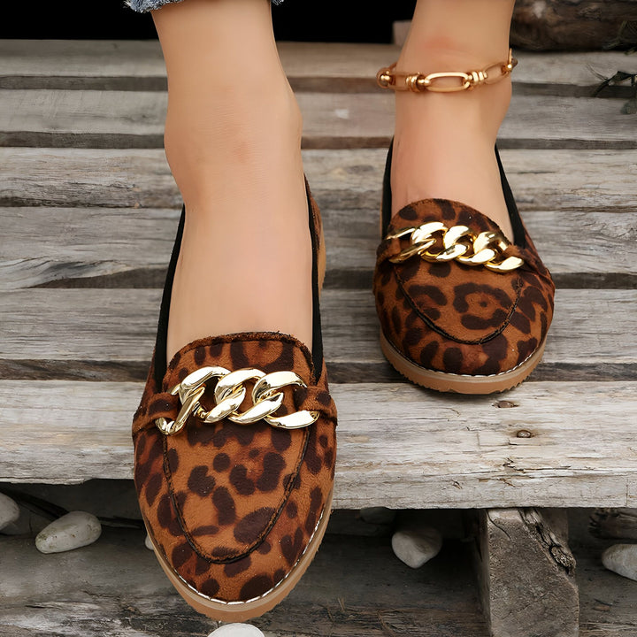 Gros plan sur des mocassins léopard avec chaînes dorées, portés par une femme sur un plancher en bois. Cheville ornée d'une chaîne dorée. Chaussures tendance et originales., 45287115030709,45287115063477,45287115096245,45287115129013,45287115161781,45287115194549,45287115227317,45287115260085