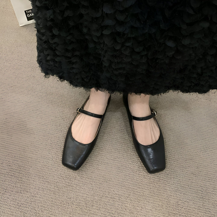 Gros plan des pieds d'une femme portant des ballerines noires à bride. Elle porte une robe noire texturée. Sols recouverts de moquette beige., 45286699761845,45286699794613,45286699827381,45286699860149,45286699892917,45286699925685,45286699958453,45286699991221,45286700023989,45286700056757,45286700089525,45286700122293