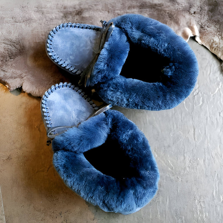 Vue rapprochée de deux chaussons en peau de mouton bleu marine, doublure intérieure douce visible, couture décorative sur le bord, lacets en cuir fins. Pose sur surface texturée neutre. Confort et chaleur., 45286951452853,45286951485621,45286951518389,45286951551157,45286951583925,45286951616693,45286951649461,45286951682229,45286951714997,45286951747765,45286951780533,45286951813301,45286951846069,45286951878837,45286951911605,45286951944373,45286951977141,45286952009909,45286952042677,45286952075445