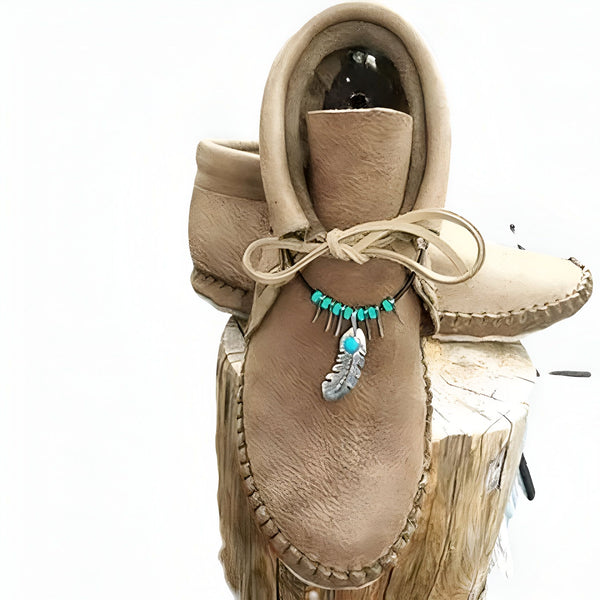 Mocassins en cuir beiges faits à la main, décorés d'un collier turquoise et d'une plume argentée. Chaussures traditionnelles amérindiennes posées sur une souche en bois. Artisanat, style bohème., 45286983499957,45286983532725,45286983565493,45286983598261,45286983631029,45286983663797,45286983696565,45286983729333,45286983762101,45286983794869,45286983827637,45286983860405,45286983893173,45286983925941,45286983958709,45286983991477,45286984024245,45286984057013,45286984089781,45286984122549,4528698
