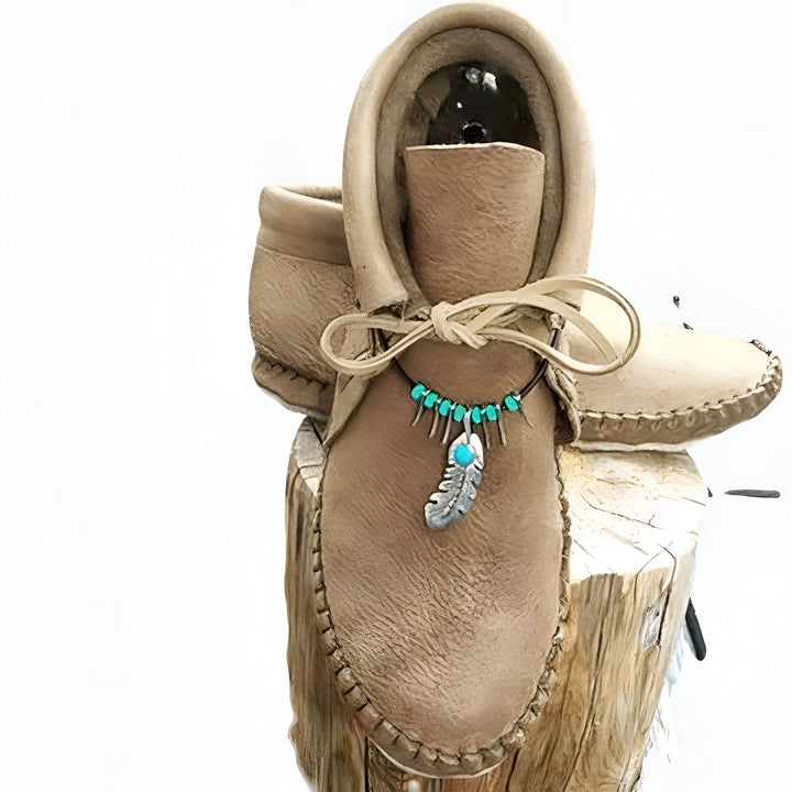 Mocassins en cuir beiges faits à la main, décorés d'un collier turquoise et d'une plume argentée. Chaussures traditionnelles amérindiennes posées sur une souche en bois. Artisanat, style bohème., 45286983499957,45286983532725,45286983565493,45286983598261,45286983631029,45286983663797,45286983696565,45286983729333,45286983762101,45286983794869,45286983827637,45286983860405,45286983893173,45286983925941,45286983958709,45286983991477,45286984024245,45286984057013,45286984089781,45286984122549,4528698