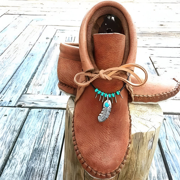 Mocassins marron en cuir avec col montant et lacets, ornés d'un collier turquoise et pendentif plume. Chaussures posées sur un tronc d'arbre rustique., 45286983499957,45286983532725,45286983565493,45286983598261,45286983631029,45286983663797,45286983696565,45286983729333,45286983762101,45286983794869,45286983827637,45286983860405,45286983893173,45286983925941,45286983958709,45286983991477,45286984024245,45286984057013,45286984089781,45286984122549,45286984155317,45286984188085,45286984220853,45286984253