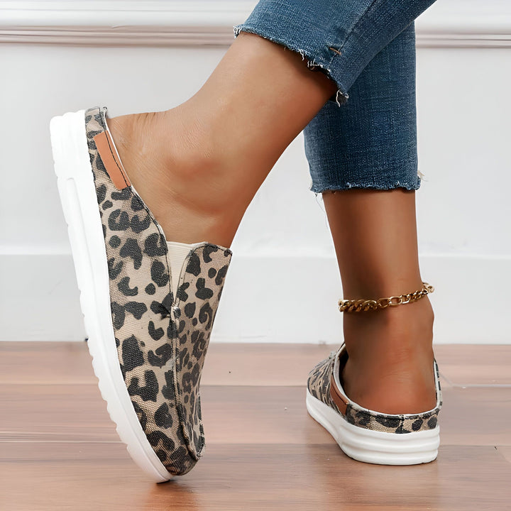 Gros plan de mules à motif léopard portées avec un jean et une chaîne de cheville dorée. Chaussures confortables et décontractées pour femmes. Mode et style., 45287151206581,45287151239349,45287151272117,45287151304885,45287151337653,45287151370421,45287151403189,45287151435957,45287151468725