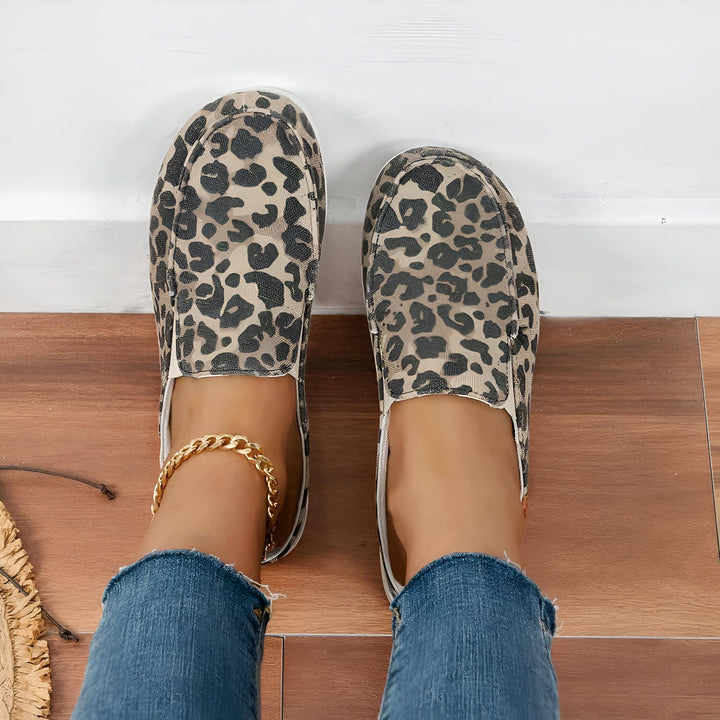 Vue de dessus des pieds d'une femme portant des chaussures à enfiler à imprimé léopard et un jean bleu, avec une chaîne de cheville dorée., 45287151206581,45287151239349,45287151272117,45287151304885,45287151337653,45287151370421,45287151403189,45287151435957,45287151468725