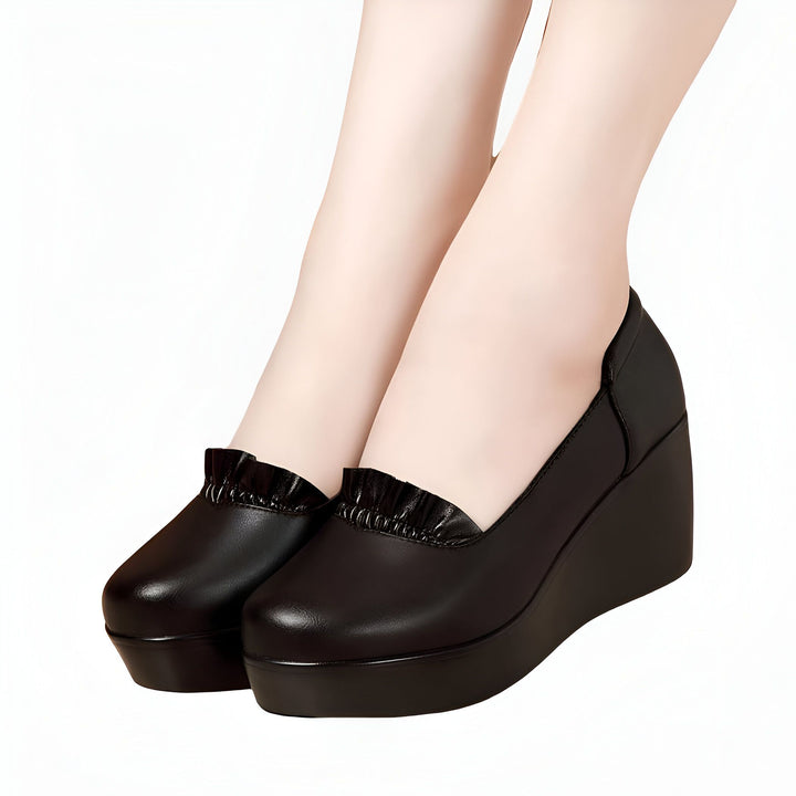 Gros plan de pieds chaussés d'escarpins compensés noirs en cuir, ornés de volants. Élégance et confort pour toutes les occasions. Chaussures à plateforme idéales pour un look tendance., 45286970032309,45286970065077,45286970097845,45286970130613,45286970163381,45286970196149,45286970228917,45286970261685,45286970294453,45286970327221,45286970359989