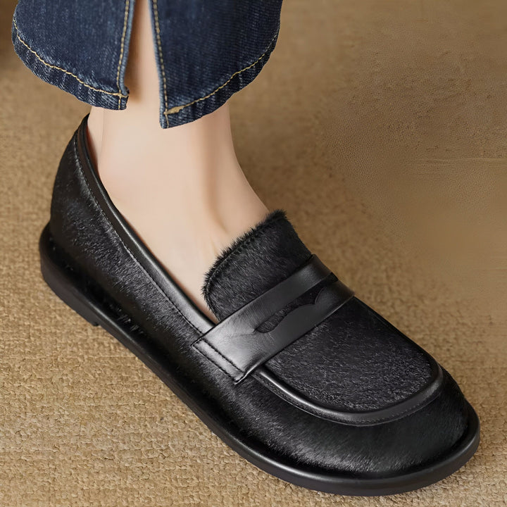 Gros plan d'un pied chaussé d'un mocassin noir à poils courts avec une bride en cuir noir. Le mocassin est porté avec un jean bleu., 45286620823733,45286620856501,45286620889269,45286620922037,45286620954805