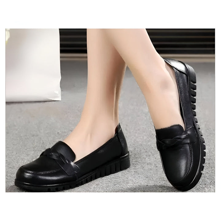 Gros plan de pieds portant des mocassins noirs en cuir, avec un détail tressé sur le dessus et une semelle à crans. Chaussures confortables et élégantes pour femme., 45286736265397,45286736298165,45286736330933,45286736363701,45286736396469,45286736429237,45286736462005,45286736494773