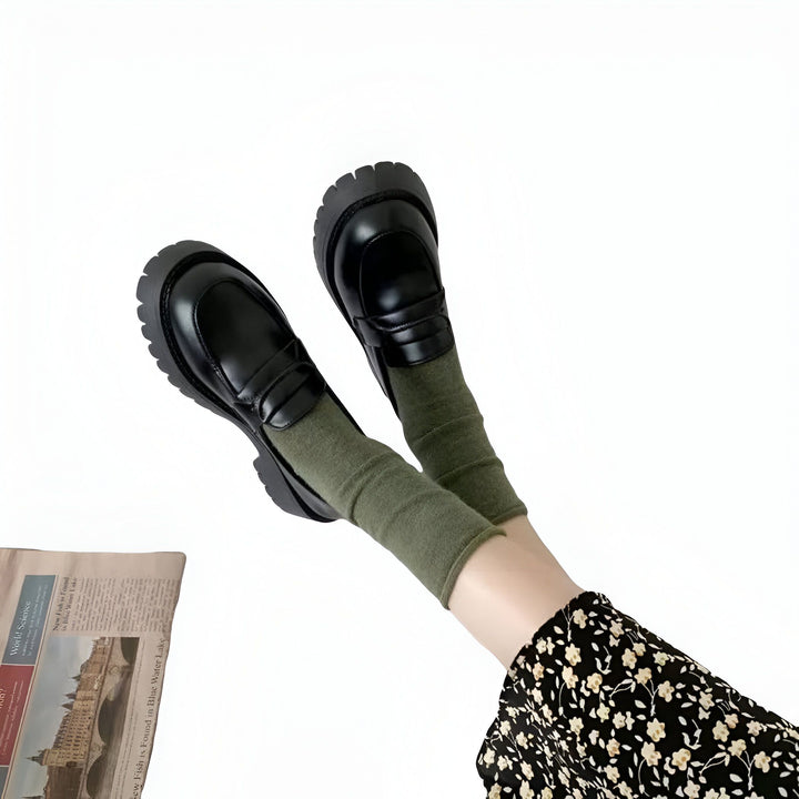 Image de mode mettant en scène une femme portant des mocassins noirs à plateforme et des chaussettes vert olive, avec une jupe à motifs floraux. Un journal est visible en arrière-plan. Style décontracté et tendance., 45286720700597,45286720733365,45286720766133,45286720798901,45286720831669,45286720864437,45286720897205,45286720929973,45286720962741