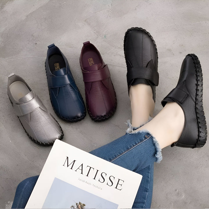 Chaussures plates en cuir pour femmes, en couleurs argent, bleu, bordeaux et noir. La personne porte le modèle noir avec un jean bleu. Livre "Matisse" visible., 45286889914549,45286889947317,45286889980085,45286890012853,45286890045621,45286890078389,45286890111157,45286890143925,45286890176693,45286890209461,45286890242229,45286890274997,45286890307765,45286890340533,45286890373301,45286890406069,45286890438837,45286890471605,45286890504373,45286890537141,45286890569909,45286890602677,45286890635445,452