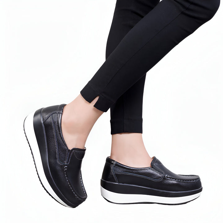 Gros plan sur des chaussures compensées noires en cuir portées avec un pantalon noir. Chaussures confortables et élégantes pour femmes., 45286901547189,45286901579957,45286901612725,45286901645493,45286901678261,45286901711029,45286901743797,45286901776565,45286901809333,45286901842101,45286901874869,45286901907637,45286901940405,45286901973173,45286902005941,45286902038709
