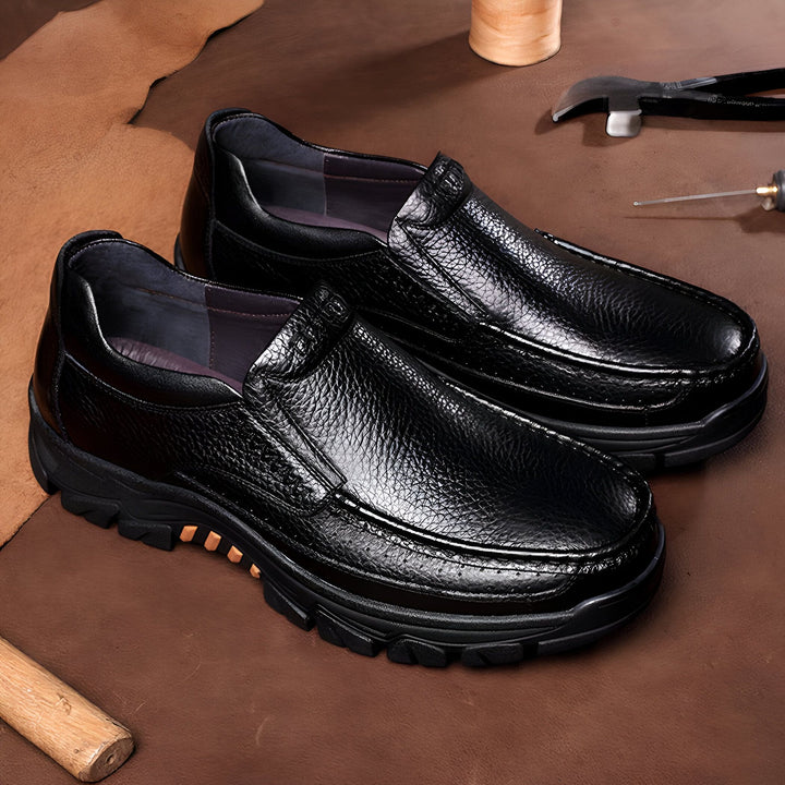 Vue rapprochée d'une paire de mocassins noirs en cuir texturé sur fond marron, entourés d'outils de cordonnerie, suggérant un artisanat de qualité. Idéal pour illustrer la mode masculine, le confort et l'élégance décontractée., 45286897352885,45286897385653,45286897418421,45286897451189,45286897483957,45286897516725,45286897549493,45286897582261,45286897615029,45286897647797,45286897680565,45286897713333