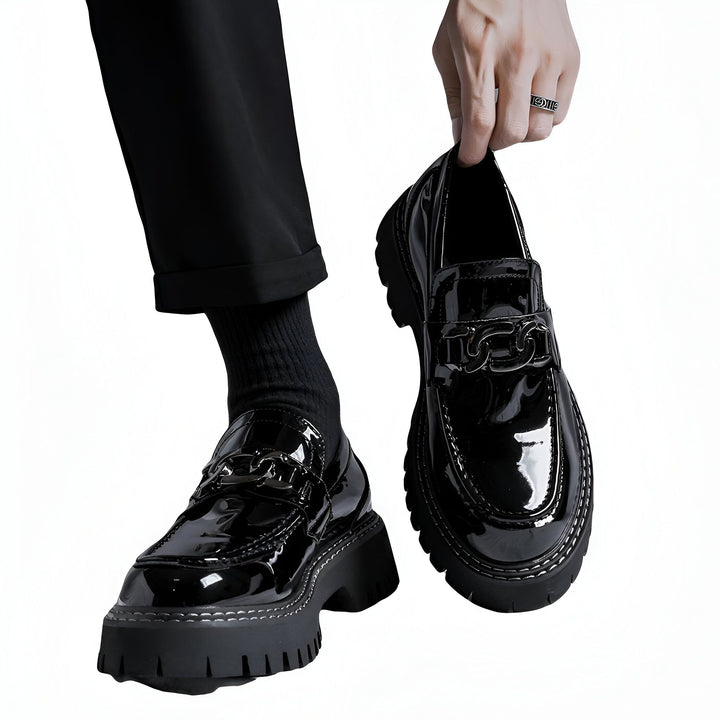 Mocassins noirs vernis à semelle épaisse et chaîne décorative. Un homme tient une chaussure à la main, l'autre au pied. Style élégant et tendance. Chaussures pour hommes, mode masculine., 45286900367541,45286900400309,45286900433077,45286900465845,45286900498613,45286900531381,45286900564149
