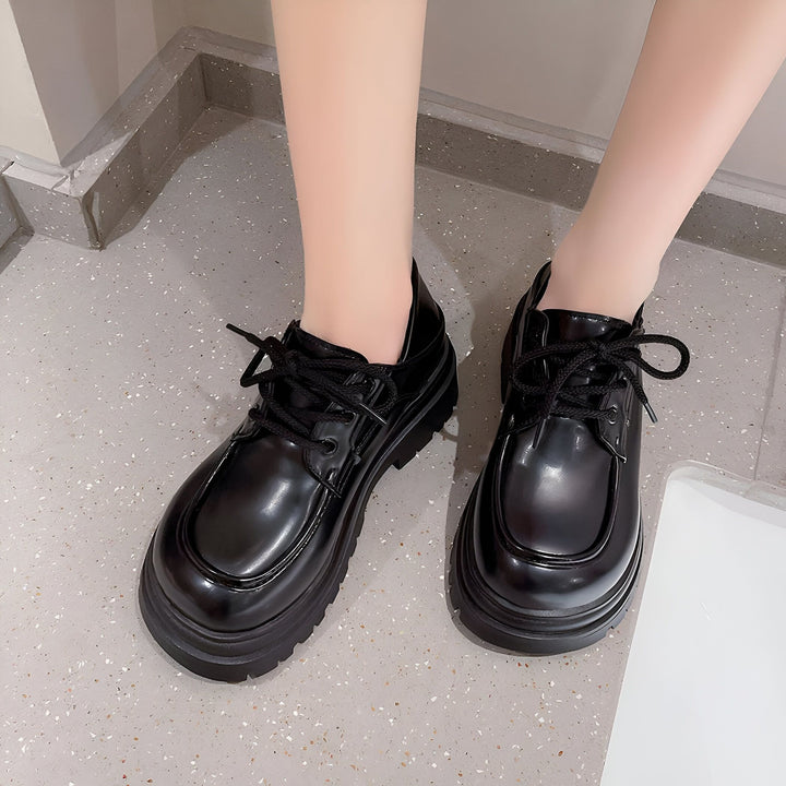 Gros plan sur des chaussures derby noires à semelles épaisses, portées par une personne sur un sol gris moucheté. Les lacets sont noirs et le cuir brillant., 45286834995381,45286835028149,45286835060917,45286835093685,45286835126453,45286835159221,45286835191989,45286835224757,45286835257525,45286835290293,45286835323061,45286835355829