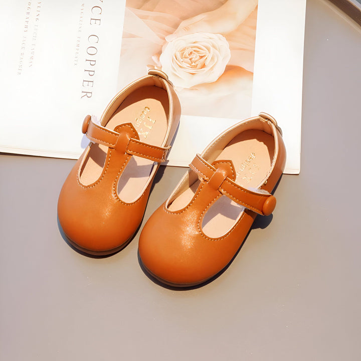 Deux chaussures pour enfants en cuir marron clair, avec bride à bouton, posées sur un magazine ouvert montrant une fleur rose. Chaussures de style Mary Jane pour filles., 45287037894837,45287037927605,45287037960373,45287037993141,45287038025909,45287038058677,45287038091445,45287038124213,45287038156981,45287038189749,45287038222517,45287038255285,45287038288053,45287038320821,45287038353589,45287038386357,45287038419125,45287038451893,45287038484661,45287038517429