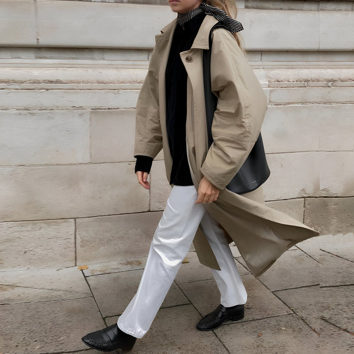 Une femme portant un trench beige, un pull noir, un pantalon blanc brillant et des mocassins noirs, avec un sac à bandoulière noir et un foulard rayé noir et blanc autour du cou., 45286895485109,45286895517877,45286895550645,45286895583413,45286895616181,45286895648949,45286895681717,45286895714485,45286895747253,45286895780021,45286895812789,45286895845557,45286895878325,45286895911093,45286895943861,45286895976629,45286896009397,45286896042165