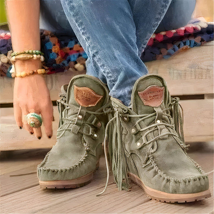 Image de bottes en daim vert olive avec franges, portées avec un jean bleu. On peut aussi voir des bracelets et une bague de style bohème. Le tout reposant sur une surface en bois, avec un fond coloré flou., 45286985236661,45286985269429,45286985302197,45286985334965,45286985367733,45286985400501,45286985433269,45286985466037,45286985498805,45286985531573,45286985564341,45286985597109,45286985629877,45286985662645,45286985695413,45286985728181,45286985760949,45286985793717,45286985826485,45286985859253