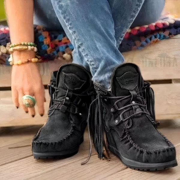 Gros plan de bottines noires à franges, portées avec un jean. On voit une main avec des bracelets et une bague turquoise. Le tout est posé sur une surface en bois. Style décontracté et bohème., 45286985236661,45286985269429,45286985302197,45286985334965,45286985367733,45286985400501,45286985433269,45286985466037,45286985498805,45286985531573,45286985564341,45286985597109,45286985629877,45286985662645,45286985695413,45286985728181,45286985760949,45286985793717,45286985826485,45286985859253,4528698589