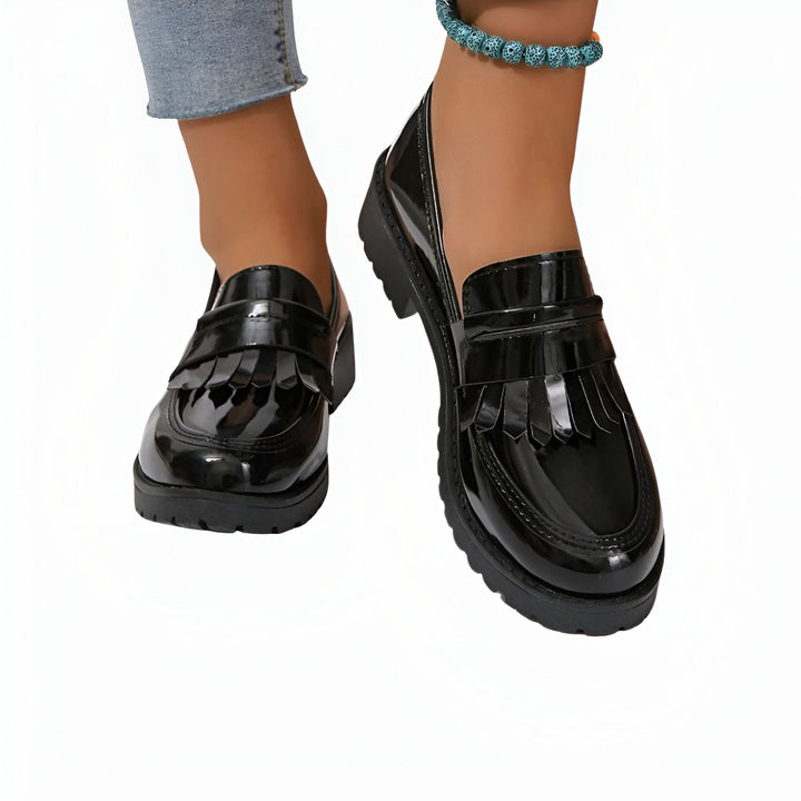 Chaussures mocassins noires vernies pour femmes, avec des franges sur le dessus. Portées avec un jean et une cheville ornée d'un bracelet de perles bleues. Style élégant et tendance., 45286687310005,45286687342773,45286687375541,45286687408309,45286687441077,45286687473845,45286687506613,45286687539381,45286687572149,45286687604917,45286687637685,45286687670453,45286687703221,45286687735989