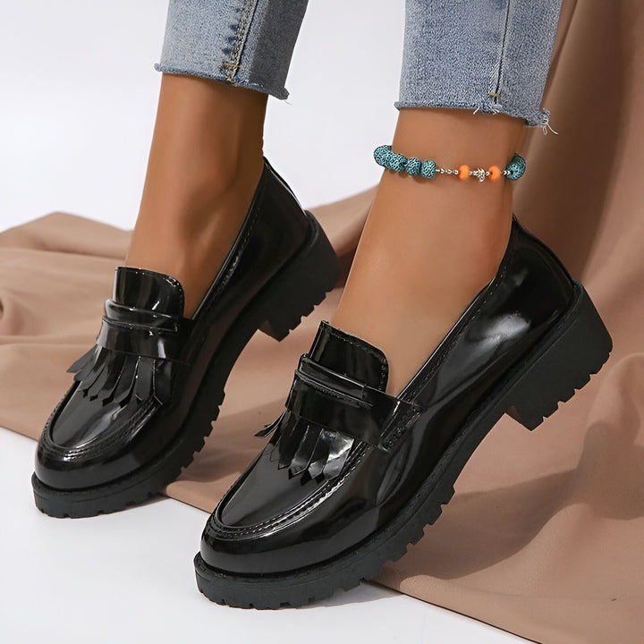 Gros plan de mocassins noirs vernis à semelles épaisses portés avec un jean et une chaîne de cheville colorée. Chaussures de mode pour femmes., 45286687310005,45286687342773,45286687375541,45286687408309,45286687441077,45286687473845,45286687506613,45286687539381,45286687572149,45286687604917,45286687637685,45286687670453,45286687703221,45286687735989