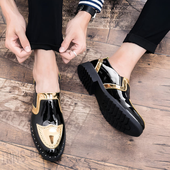 Gros plan sur des mocassins noirs vernis avec des détails dorés portés par un homme ajustant son pantalon noir sur un sol en bois. La montre et la chemise rayée ajoutent une touche élégante., 45287058735285,45287058768053,45287058800821,45287058833589,45287058866357,45287058899125,45287058931893,45287058964661,45287058997429,45287059030197