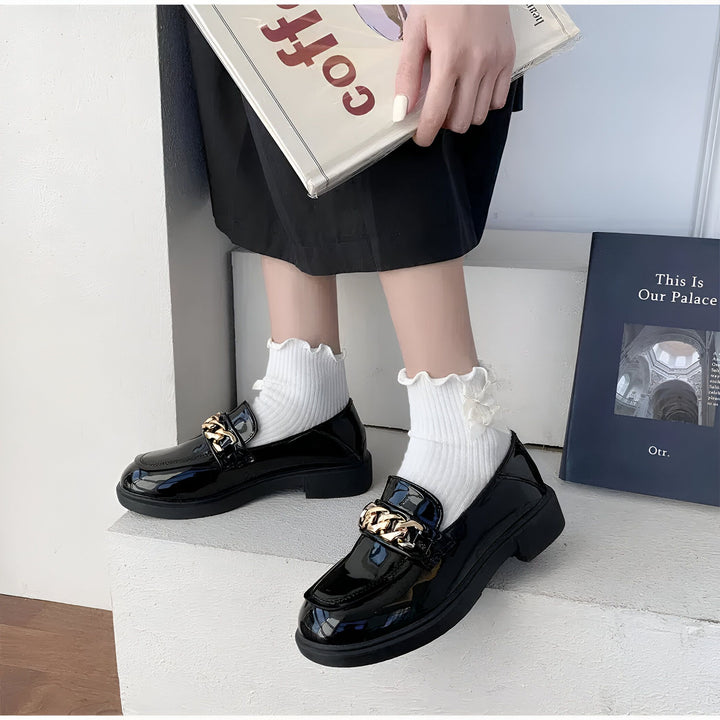 Gros plan de mocassins noirs vernis avec chaîne dorée portés avec des chaussettes blanches à volants. Mains tenant un livre "Coff". Style preppy, chaussures tendance., 45287065419957,45287065452725,45287065485493,45287065518261,45287065551029,45287065583797