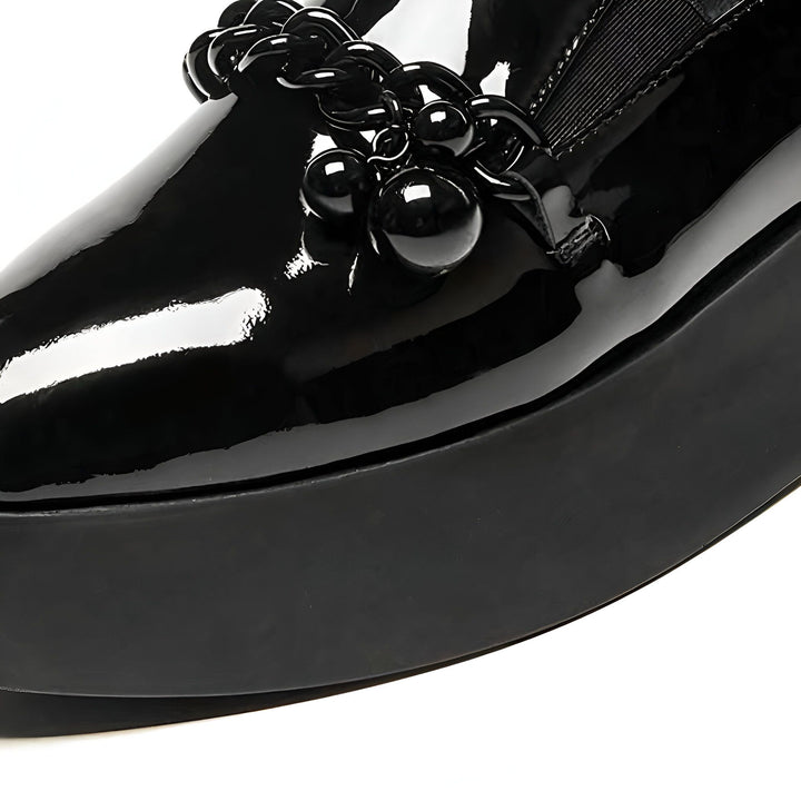 Gros plan sur une chaussure vernie noire à plateforme, ornée d'une chaîne et de grosses perles noires décoratives. Style audacieux et moderne., 45286905544885,45286905577653,45286905610421,45286905643189,45286905675957,45286905708725,45286905741493