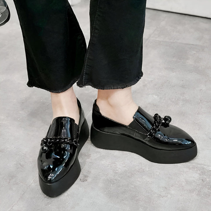 Gros plan sur des mocassins vernis noirs à plateforme avec des chaînes décoratives, portés avec un jean noir décontracté. Chaussures de mode élégantes., 45286905544885,45286905577653,45286905610421,45286905643189,45286905675957,45286905708725,45286905741493